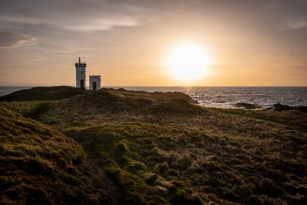 A lighthouse on grassy cliffs at sunset over the ocean.